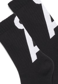 Schwarze Socken aus einem strukturierten Strickmaterial mit einem auffälligen weißen Grafikdesign. Die Gesamtform ist standardmäßig mit einem bequemen Sitz.