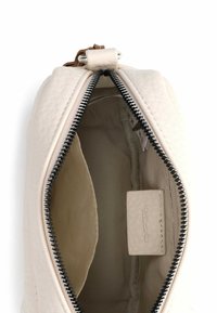 Kremowa, teksturowana saszetka na zamek z ciemnym suwakiem. Wnętrze wyłożone jest gładką podszewką z widoczną metką. Kompaktowy, zaokrąglony kształt.