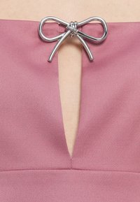 Frambozenroze jurk met een diepe V-hals, benadrukt door een zilveren metallic strikdetail in het midden, met een soepele textuur.