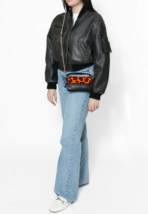 Zwarte leren bomberjack met geribde manchetten, lichtblauwe uitlopende jeans en een kleine schoudertas met een oranje en zwart luipaardpatroon.