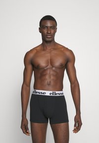 Schwarze Boxershorts mit einem weißen "ellesse" Logo-Bund. Das Material wirkt glatt, eng anliegend und dehnbar, mit einem schlichten Design.