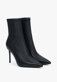 Zwarte leren enkellaarsjes met een strakke pasvorm, een spits toelopende neus en een stilettohak. Gladde textuur met minimale stikseldetails.