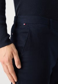 Pantaloni blu navy realizzati in tessuto liscio, con tasche laterali e un piccolo dettaglio del logo rosso, bianco e blu sulla vita.