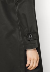 Svart vattentät kappa med knäppt manschett med kviltade detaljer, slät textur och en figurnära design.