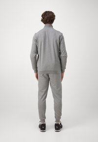 Ensemble de survêtement gris avec une veste à zip et un pantalon assorti. Comprend des poignets et un ourlet côtelés, une texture douce, et est associé à des chaussures de sport noires.