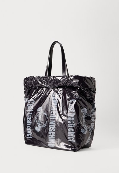 Geantă de tote neagră, lucioasă, cu margine superioară plisată, două mânere negre și text imprimat în gri deschis care spune "C'est trash chic!" și detalii de logo.
