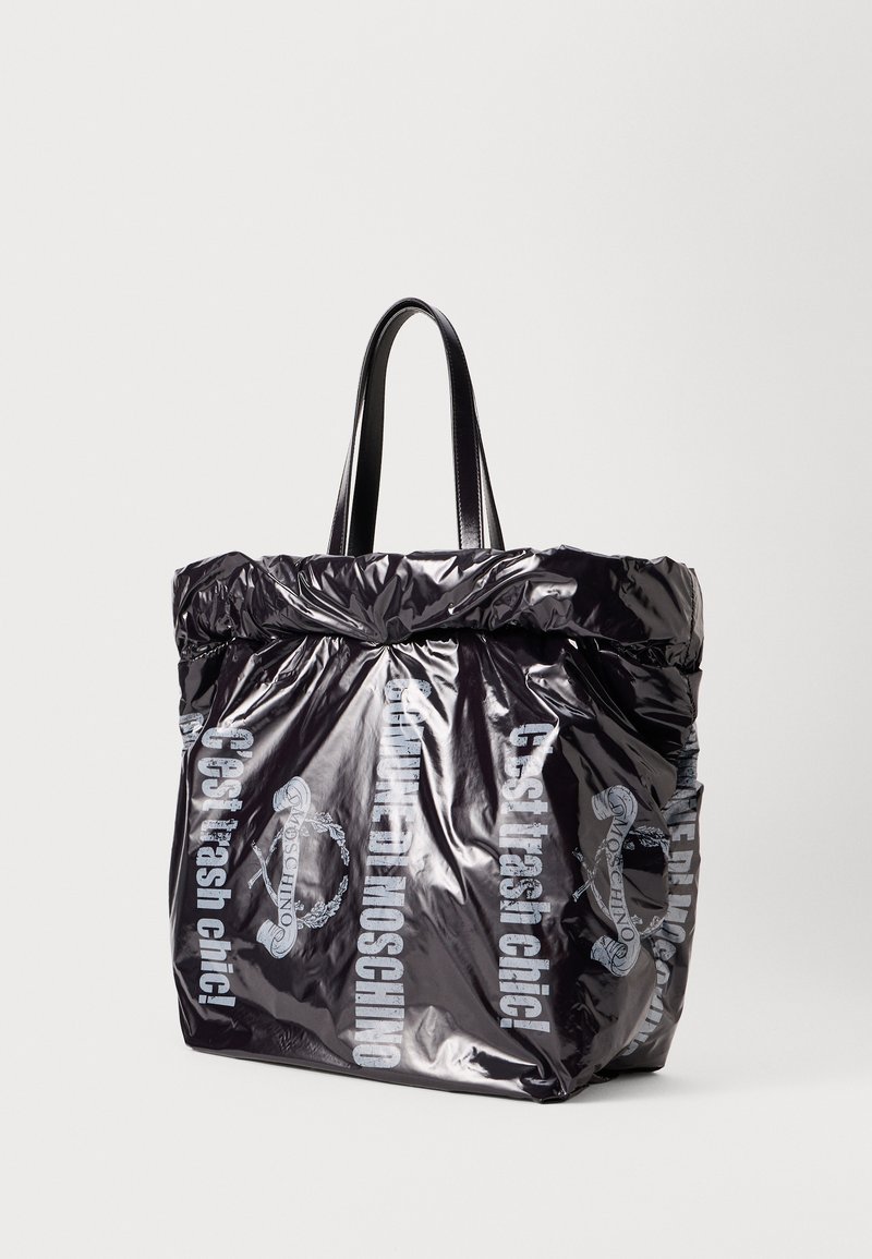Borsa tote nera e lucida con bordo superiore arricciato, doppi manici neri e testo stampato in grigio chiaro che dice "C'est trash chic!" e dettagli del logo.