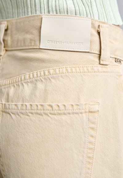 Jean en denim beige avec une texture lisse, présentant une étiquette en cuir sur la taille et des poches arrière classiques dans un design à coupe classique.