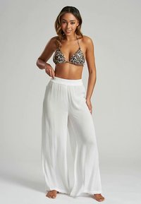 Top de bikini con estampado de leopardo y tirantes delgados, combinado con pantalones sueltos, blancos y ligeros, de cintura alta y piernas anchas.