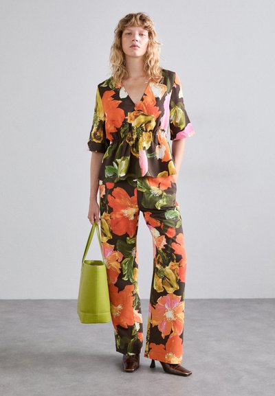 Top și pantaloni cu imprimeu floral în nuanțe de maro, portocaliu, roz și verde. Topul are un design peplum; asortat cu o geantă verde și tocuri maro.