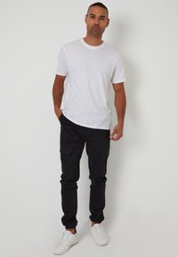 Weißes T-Shirt mit kurzen Ärmeln, kombiniert mit schwarzen Cargo-Hosen. Das Outfit wird mit weißen Sneakers abgerundet und die Hose verfügt über elastische Bündchen.