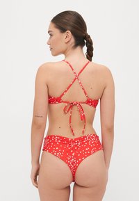Röd blommig bikini med justerbara korsryggsremmar och knyt bak. Högmidjad underdel med rynkad textur och vita blommönster.