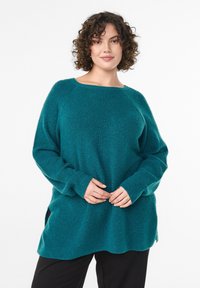 Teal knit sweater with a loose fit, wide neckline, and long sleeves. Features ribbed texture and side slits at the hem.