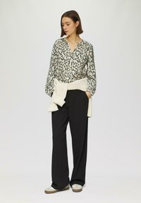 Chemisier à manches longues avec un motif géométrique multicolore, associé à un pantalon noir ample et un pull en tricot crème noué à la taille.