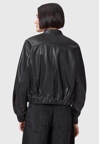 Giubbotto bomber in pelle nera con vita elastica aderente, texture liscia, colletto arrotondato e polsini arricciati, caratterizzato da un design minimalista.