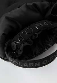 Sort nylon taske med en indsnøret åbning, der har en struktureret sort rem prydet med "POLARN O. PYRET" og en knapdetalje.