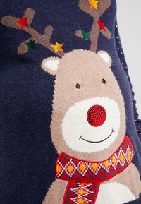 Pull bleu marine présentant un renne brodé avec un nez rouge et une écharpe décorative, orné d'étoiles colorées sur les bois.