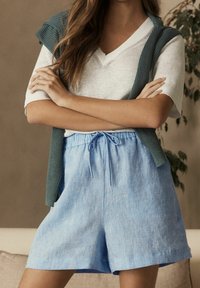 Jasnoniebieskie lniane szorty z elastycznym paskiem i sznurkiem. Połączone z szarą, prążkowaną kamizelką bez rękawów i białym t-shirtem.
