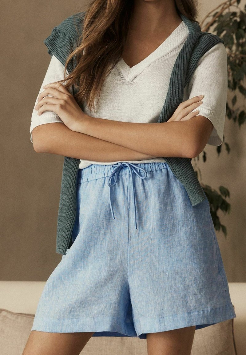 Jasnoniebieskie lniane szorty z elastycznym paskiem i sznurkiem. Połączone z szarą, prążkowaną kamizelką bez rękawów i białym t-shirtem.