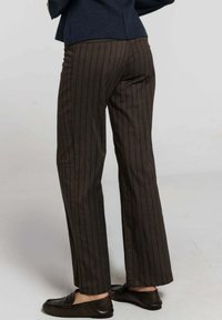 Pantalons rayés marron et foncé, de forme évasée, en tissu doux, avec des poches latérales, associés à des mocassins foncés, vus de l'arrière.