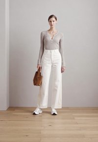 Hellgraues, geripptes Langarmoberteil, hoch taillierte weiße weit geschnittene Hose, weiße Sneakers und eine braune Handtasche. Minimalistisches Design und neutrale Farben.