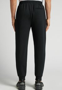 Czarne, sportowe spodnie dresowe z elastycznym pasem, zwężanymi mankietami i tylną kieszenią. Gładki materiał z lekko teksturowanym wykończeniem.