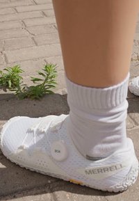 White Merrell athletic shoe with perforated texture, Boa lacing system, and yellow rubber sole, paired with a white sock on a paved surface.