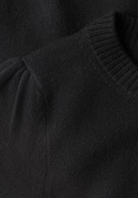 Gros plan d'un pull noir en maille montrant un col rond côtelé et un tissu texturé avec un léger froncement à la couture d'épaule.