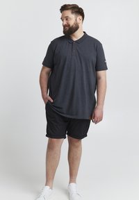 Camisa polo gris con una tapeta de dos botones, combinada con pantalones cortos negros. Zapatillas blancas completan el conjunto. Diseño simple y corte relajado.