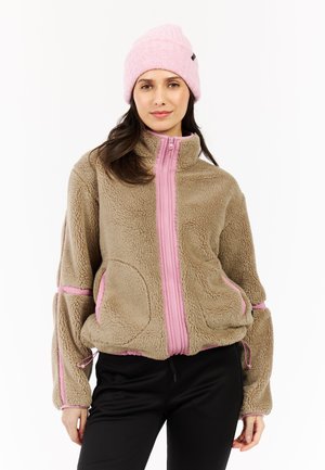 Bruine fleece jacket met roze ritsen en accenten, voorzien van grote zakken, hoge kraag en verstelbare zoom. Gecombineerd met een roze gebreide beanie.