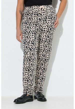 Osoba ubrana w beżowe spodnie w panterkę z troczkiem w talii, czarne wsuwane buty i czarną bluzkę, stojąca z rozluźnionymi rękami.