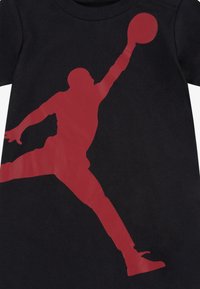 Černé bavlněné tričko s velkým červeným siluetou basketbalisty v skákací pozici, s krátkými rukávy a kulatým výstřihem.