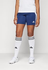 Blå atletiske shorts med hvite side-striper, kombinert med hvite knesokker med svarte striper. Hvite fotballsko fullfører antrekket.