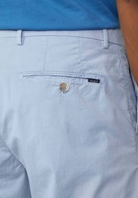 Shorts bleu clair en coton avec une poche arrière, dotés d'une fermeture à bouton et d'une étiquette de marque « HACKETT ». Texture lisse.