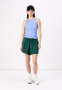 Top senza maniche blu chiaro con logo GAP, abbinato a pantaloni corti verdi larghi con cordoncino. Indossato con sneakers bianche alte e un cappellino nero.