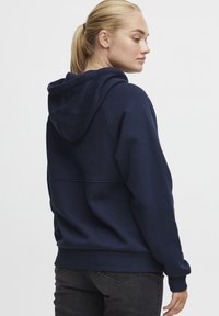 Navy blue hoodie in soft fabric with a drawstring hood, ribbed cuffs and hem, featuring a seam detail across the back.