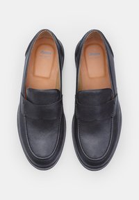 Mocasines de cuero negro con una textura suave, punta redondeada y un pequeño detalle bordado en la parte superior. Plantilla etiquetada como "Cuero Real Bata".