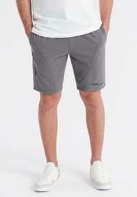 Shorts de sport gris au tissu lisse, avec des coutures contrastées, des poches latérales et des accents imprimés sur la jambe gauche.