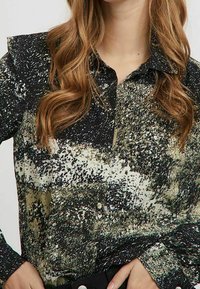 Svart och grön mönstrad blus med kragdetalj, texturerad tyg och knappar, som har abstrakta mönster och en avslappnad passform.