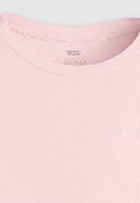 Lichtroze katoenen t-shirt met een ribgebreide ronde hals en een klein wit Levi's-logo gestikt aan de linkerkant. Zachte textuur en minimalistisch ontwerp.