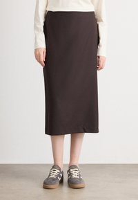 Jupe de maternité en tissu marron foncé, longueur genoux avec un design droit et épuré. Associée à des baskets grises avec une surface texturée.