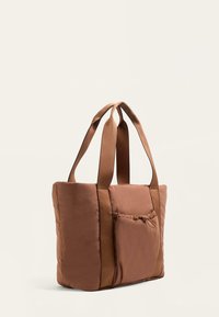 Bruine gevoerde totebag met twee handvatten aan de bovenkant, voorzien van een voorvak met een trekkoordsluiting. Gladde textuur en rechthoekige vorm.