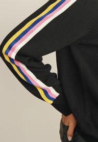 Zwarte gebreide trui met een slim-fit ontwerp. De mouwen hebben horizontale strepen in blauw, roze, wit en geel. Zachte textuur, casual stijl.