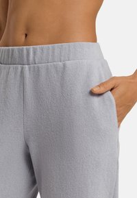 Lichtgrijze joggingbroek van gestructureerde stof, met een elastische tailleband en zijzak, gezien van de taille tot halverwege de dij.