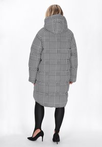Fekete-fehér kockás puffertól, kapucnival, steppelt mintázattal és hosszú ujjakkal. Fekete leggings-szel és magassarkúval párosítva.