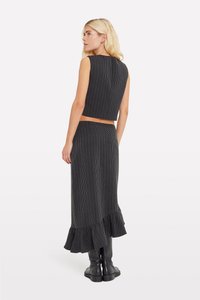 Compleu din două piese, cu tricot negru ribat, care include un top scurt fără mâneci și o fustă lungă cu tiv răsfrânt. Asortat cu cizme negre până la genunchi.