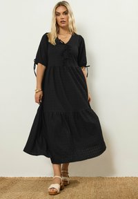 Vestido maxi negro en capas con escote en V, mangas cortas con lazos, tejido texturizado, que presenta un corte relajado y longitud por debajo de la rodilla.