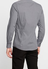 Černobílá košile s dlouhým rukávem a mikro tečkovaným vzorem. Má límec a manžety na knoflíky, slim-fit střih a hladkou texturu.