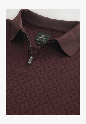 Burgundy värvi polo särk, millel on tõmbluku kaelus, tekstuuriga geomeetriline muster ja sildiga, mis näitab suurust keskmine, bränd Next ja tavaline lõige.