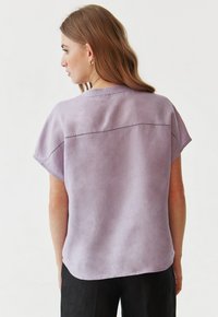 Korte mouw lavendelkleurige blouse met een ronde hals en decoratieve stiksels op de achterkant, gemaakt van een zachte, gestructureerde stof.